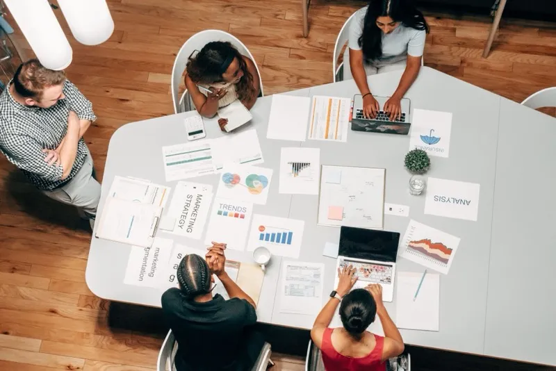 A team working together around a table covered in marketing strategy, trend and analysis sheets